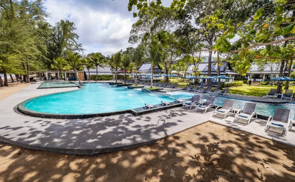Piscine bordée de transats dans un cadre tropical et ensoleillé.