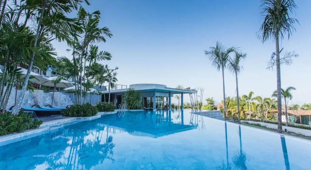 Une piscine rectangulaire bordée de transats et de végétation tropicale.