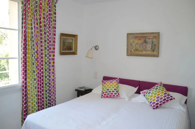 Une chambre lumineuse avec un lit recouvert d'une courtepointe blanche et de coussins colorés.