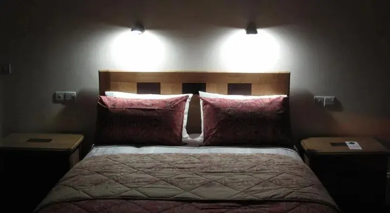 Un lit double avec des oreillers rouges dans une chambre éclairée par des lampes murales.
