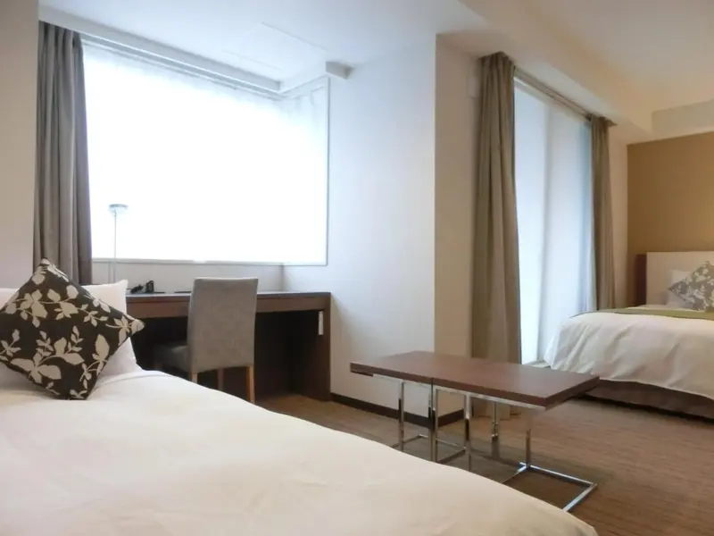 Une chambre lumineuse avec deux lits simples et un bureau près de la fenêtre.