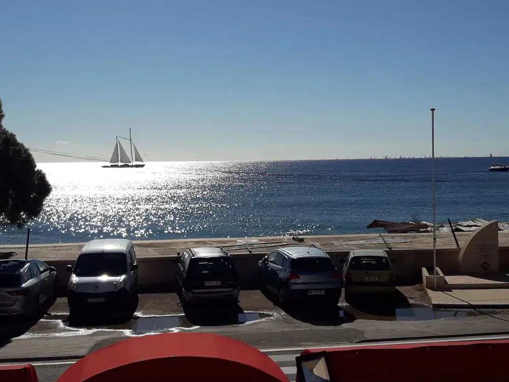 Voitures garées le long d'une promenade face à la mer scintillante sous le soleil.
