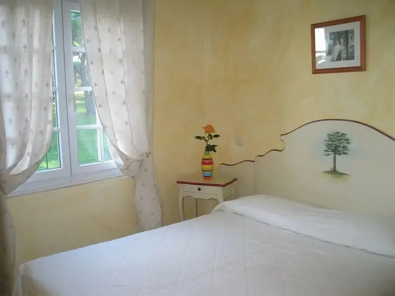 Une chambre lumineuse avec un lit recouvert d'une courtepointe blanche et une fenêtre donnant sur un jardin.