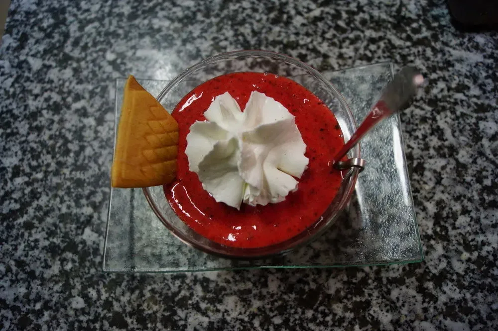 Une coupe de dessert à la fraise surmontée de crème fouettée et accompagnée d'un biscuit.