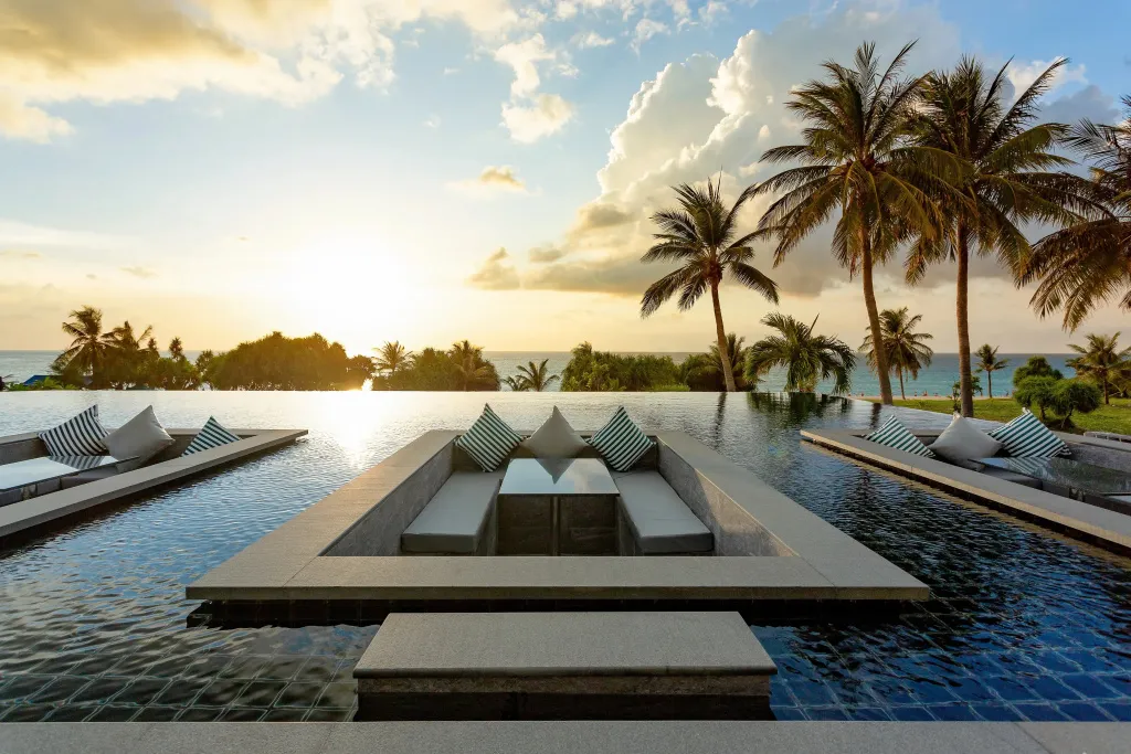 Une piscine à débordement avec des salons confortables et une vue sur la mer au coucher du soleil.
