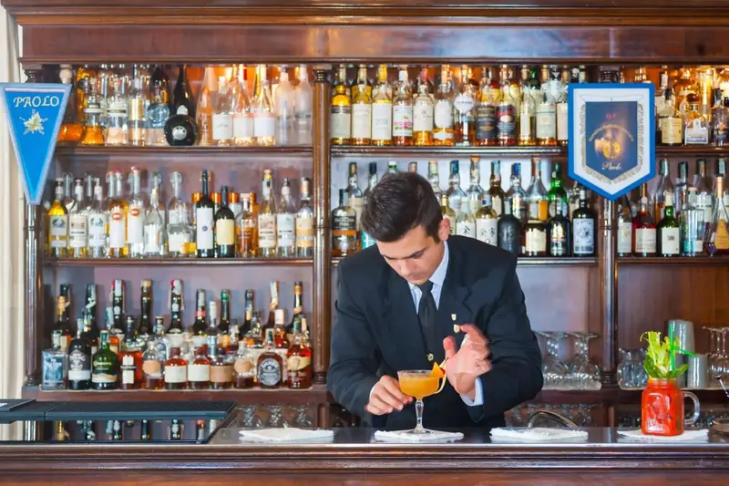 Un barman prépare un cocktail devant un comptoir bien garni de bouteilles.