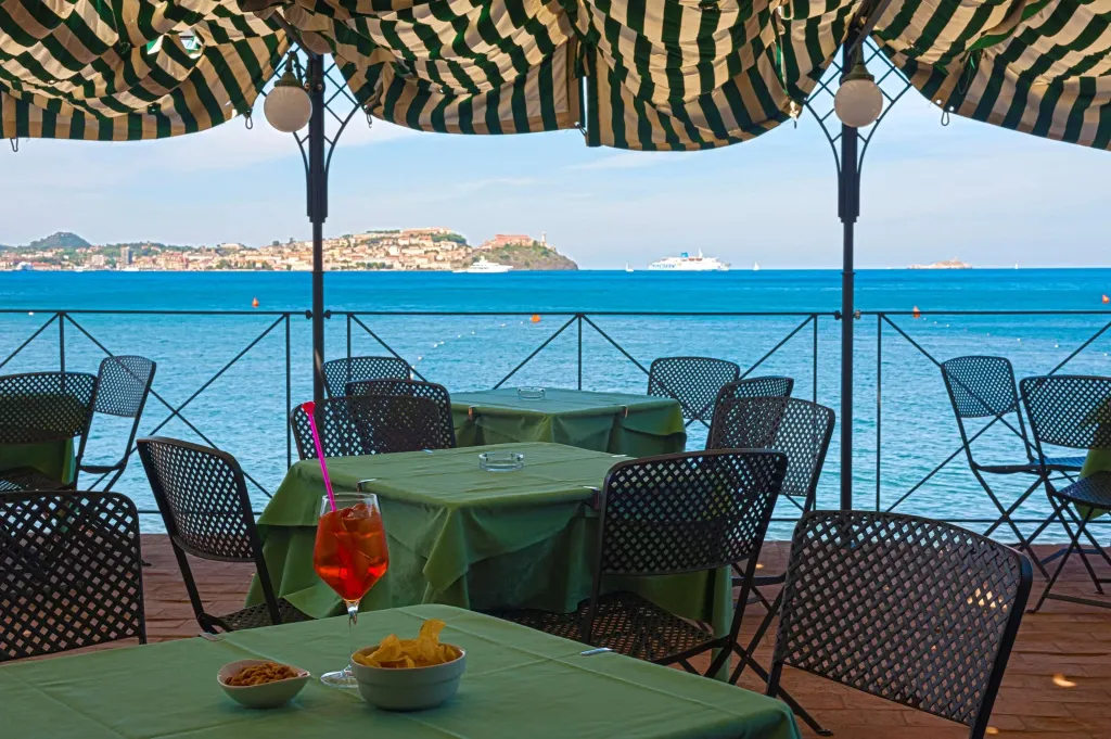 Tables et chaises vertes disposées en terrasse avec vue sur la mer et la côte.