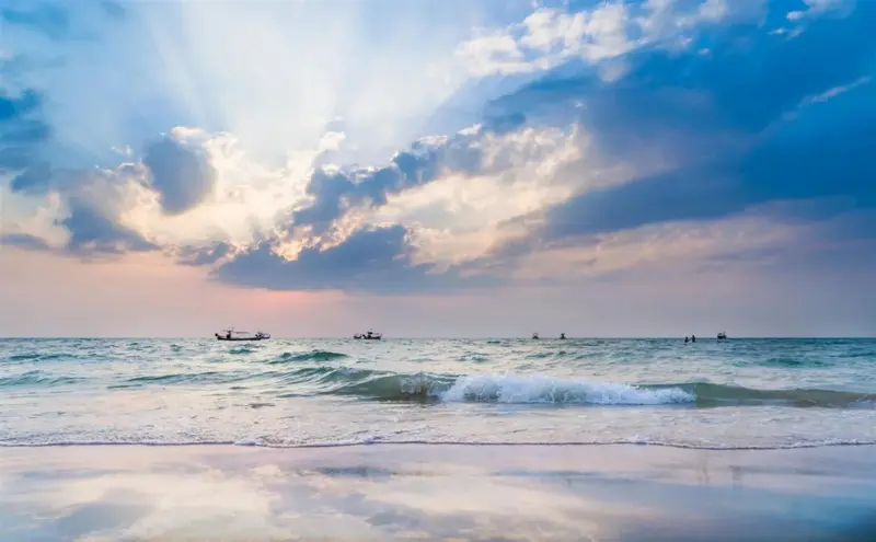 Vague déferlant sur une plage de sable fin sous un ciel nuageux et lumineux.