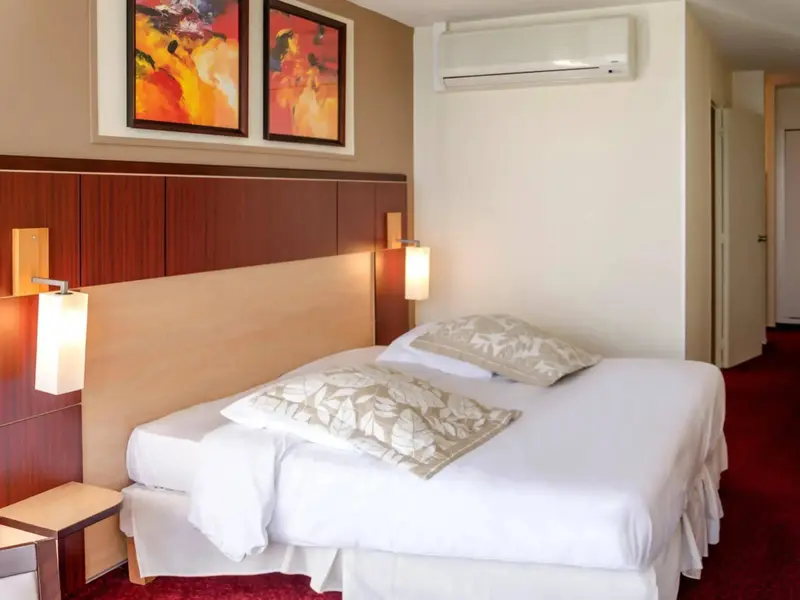 Une chambre lumineuse avec un grand lit recouvert d'une courtepointe blanche et de coussins.