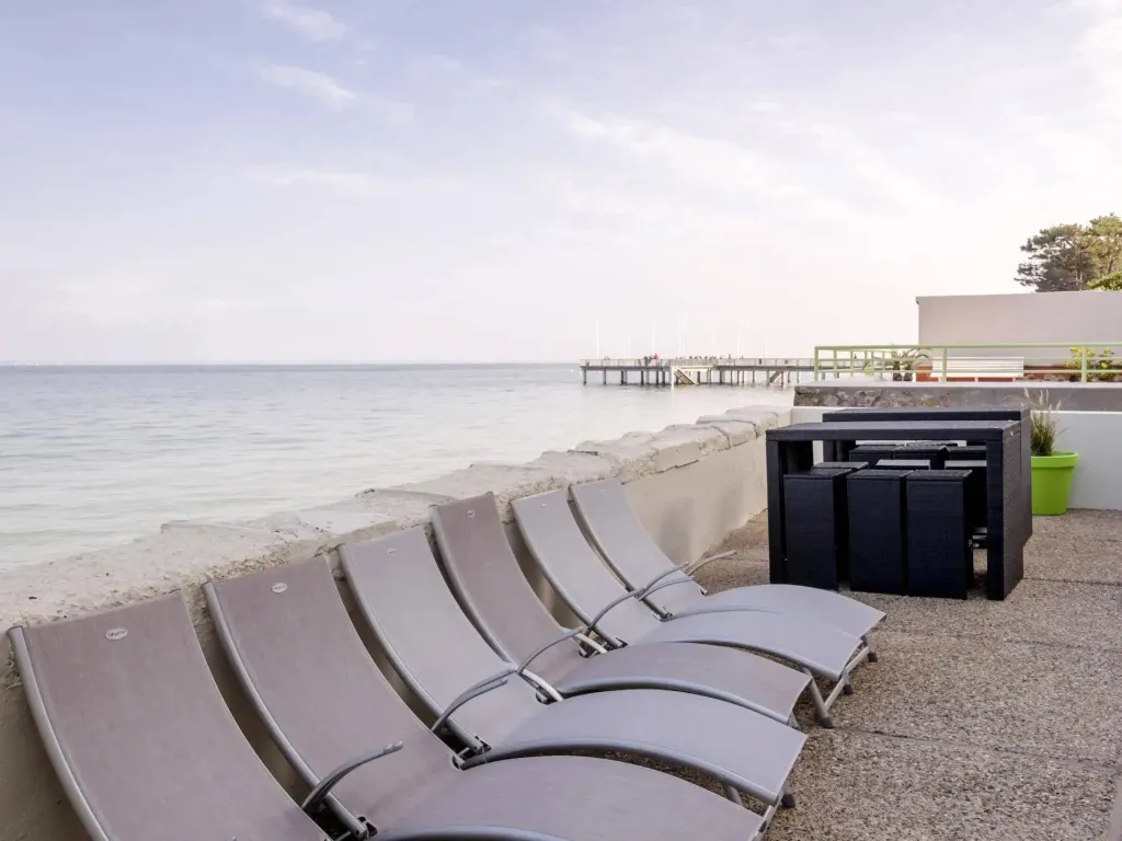 Transats alignés sur une terrasse ensoleillée face à la mer.