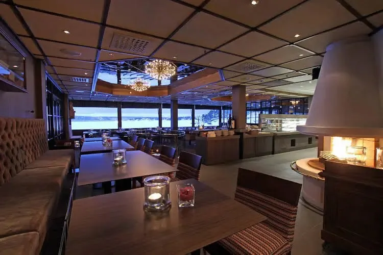 Une salle lumineuse avec des tables et des banquettes face à une grande baie vitrée.