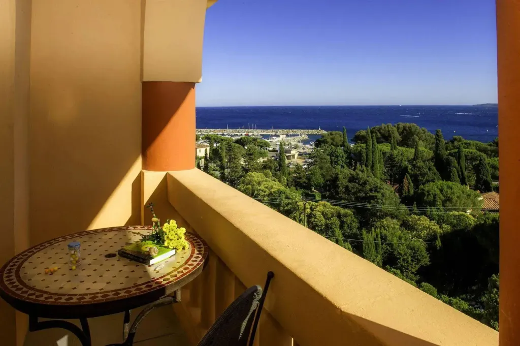 Une table ronde avec une composition florale sur une terrasse ensoleillée offre une vue sur la mer et la végétation.