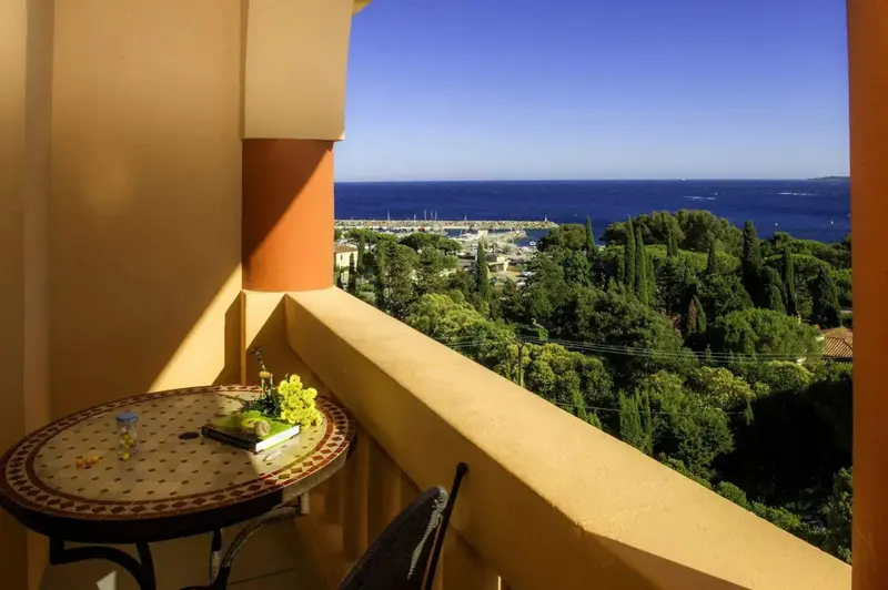 Une table ronde avec une composition florale sur une terrasse ensoleillée offre une vue sur la mer et la végétation.