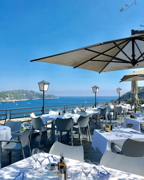 Tables dressées en terrasse avec vue sur la mer et les collines.
