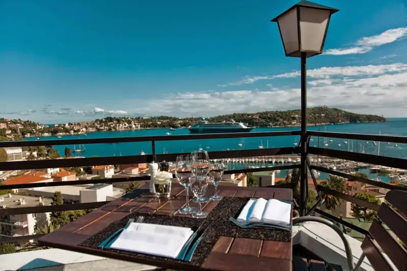 Une table dressée sur une terrasse offre une vue sur la mer et la côte.