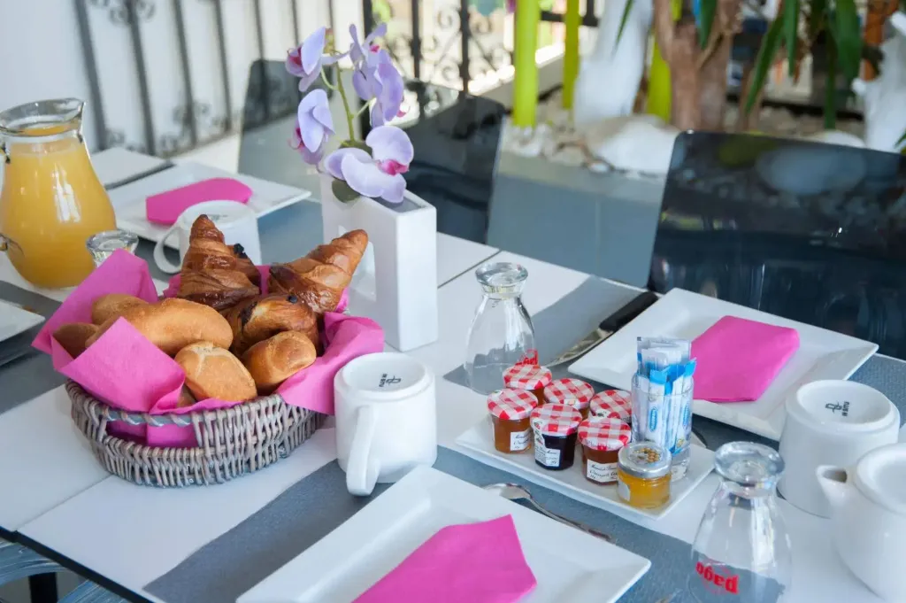 Une table est dressée avec des viennoiseries, des confitures et des boissons.