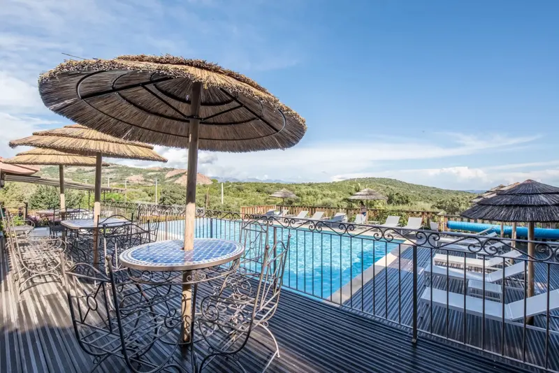 Terrasse avec tables et parasols surplombant une piscine ensoleillée.