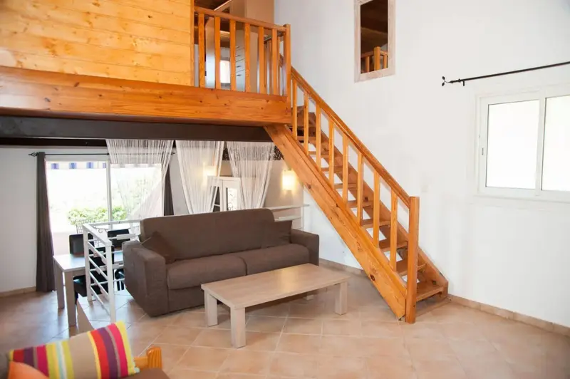 Un salon lumineux avec un canapé et une table basse, donnant sur une mezzanine en bois.