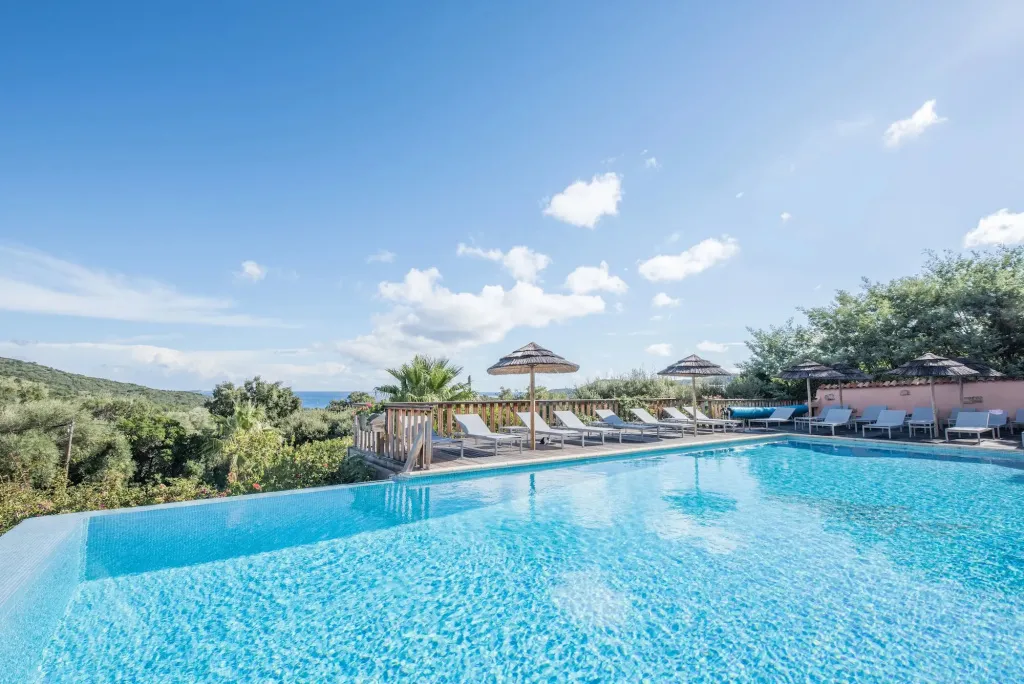 Une piscine à débordement avec des transats et des parasols offre une vue sur la mer et la végétation.