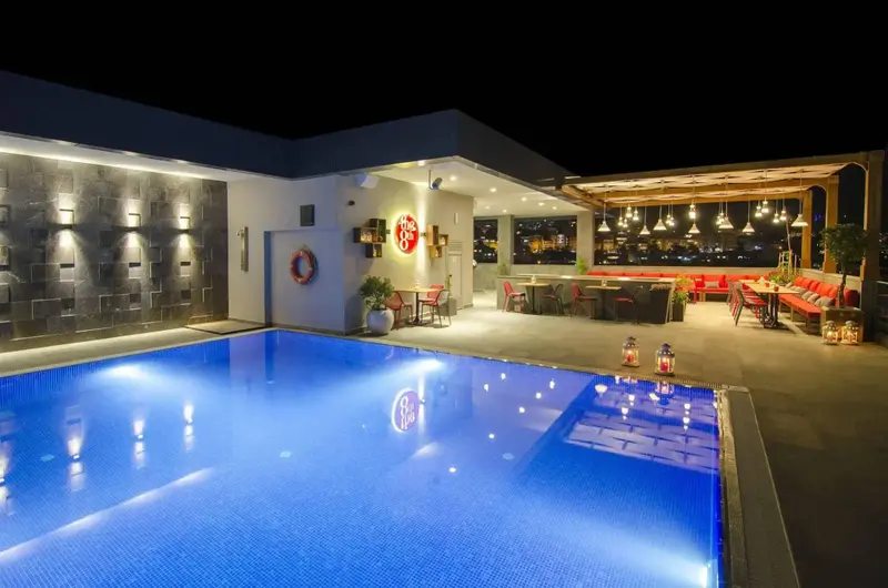Une piscine illuminée avec un espace bar et salon en arrière-plan.