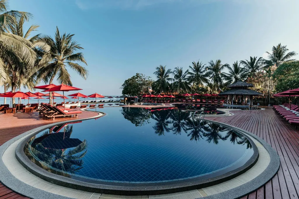 Une piscine bleue bordée d'une terrasse en bois avec des transats rouges et des parasols.