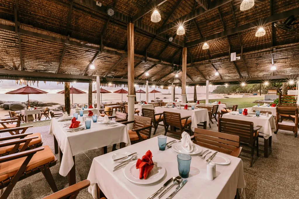 Une salle à manger extérieure avec des tables dressées face à la mer.