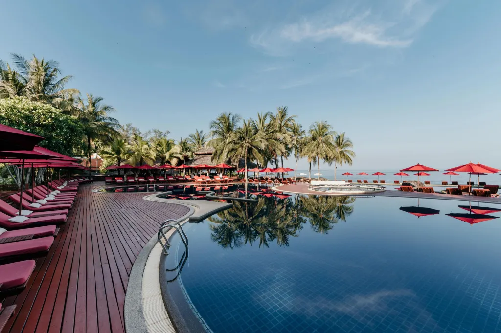 Une piscine bordée d'une terrasse avec des transats rouges sous des parasols.