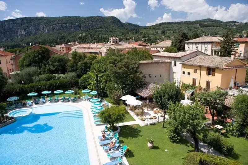 Vue aérienne d'une piscine turquoise entourée de transats et d'un jardin verdoyant.
