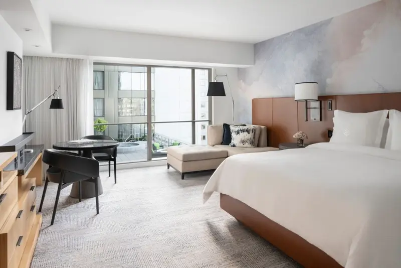 Une chambre lumineuse avec un grand lit et un coin salon près d'une baie vitrée.