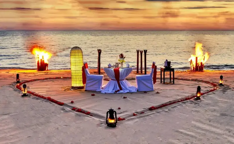 Table romantique dressée sur une plage au coucher du soleil.