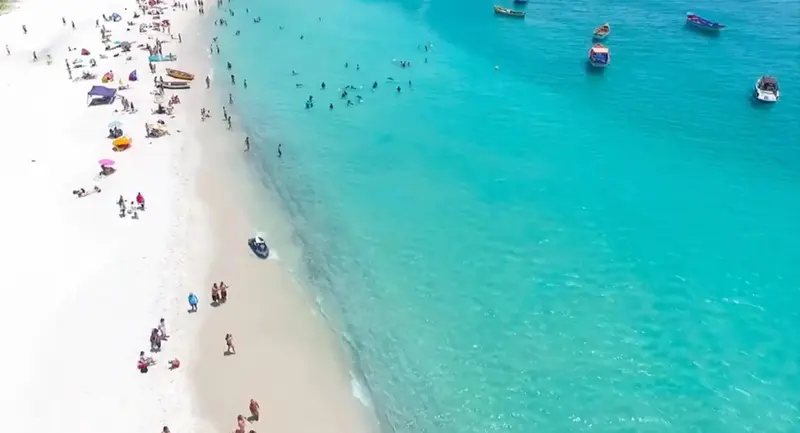 Vue aérienne d'une plage de sable blanc bordée d'une eau turquoise et de quelques embarcations.