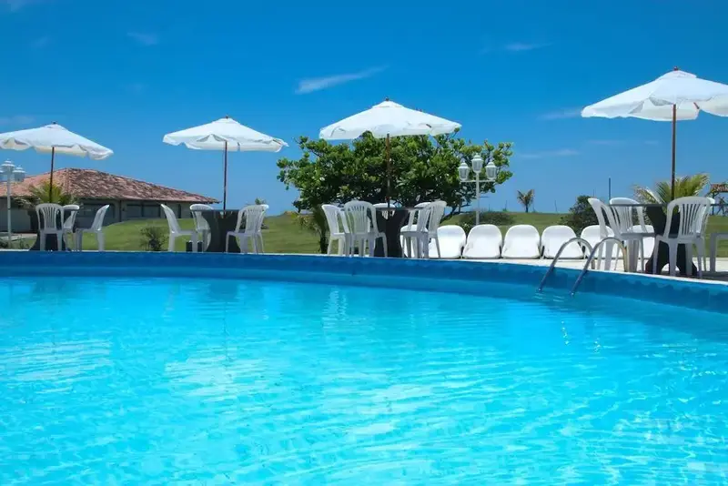 Une piscine bordée de chaises longues et de parasols blancs sous un ciel bleu dégagé.