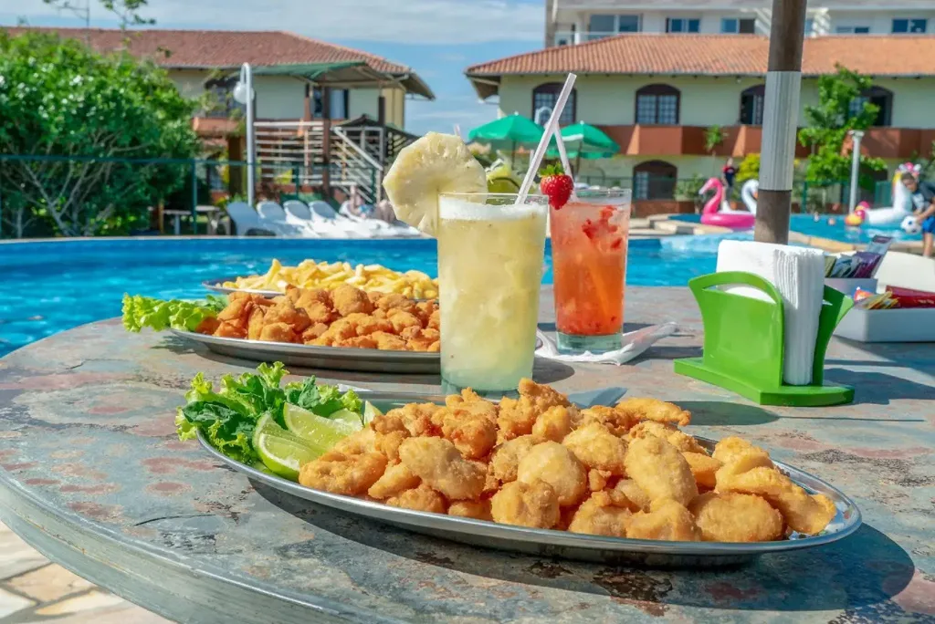 Assiettes de friture et boissons colorées sur une table au bord d'une piscine ensoleillée.