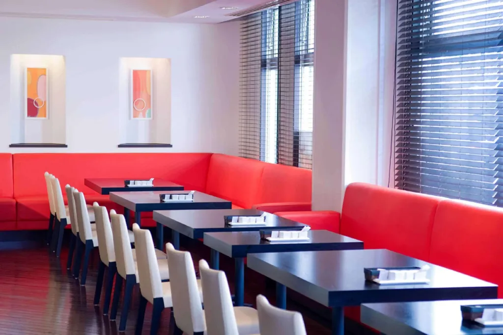 Une salle de restaurant lumineuse avec des banquettes rouges et des tables bleues.