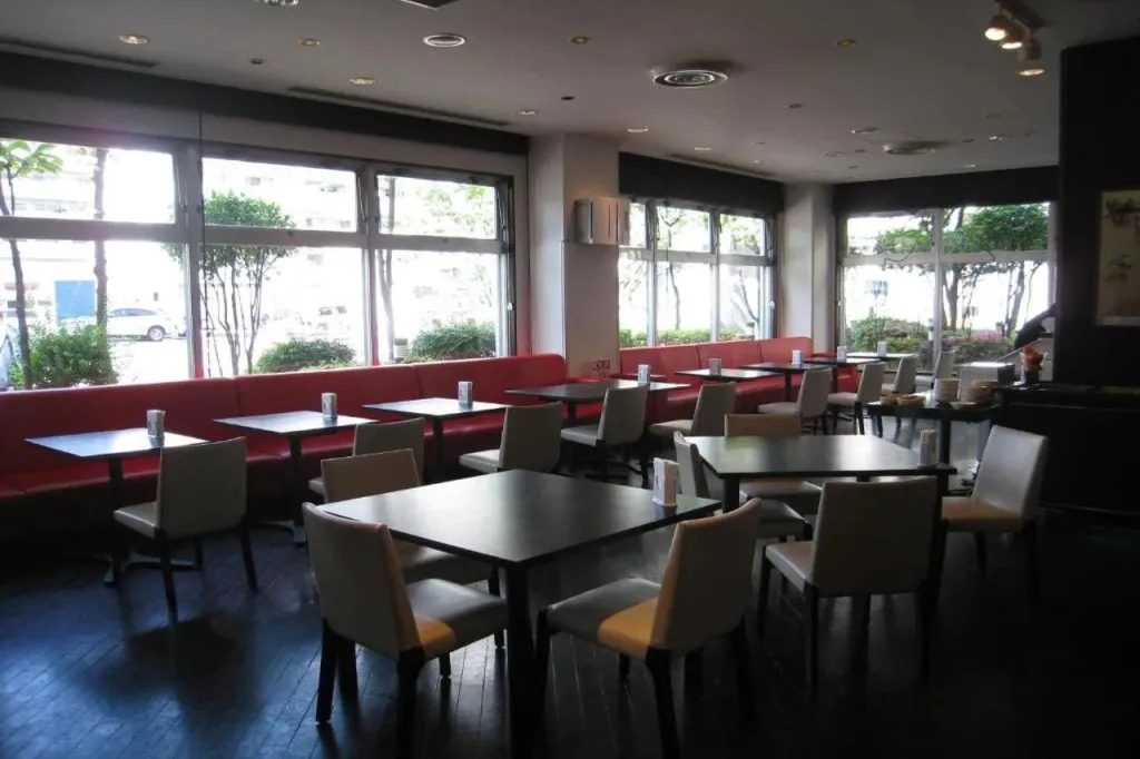 Une salle lumineuse avec des tables et des chaises est disposée devant de grandes fenêtres.