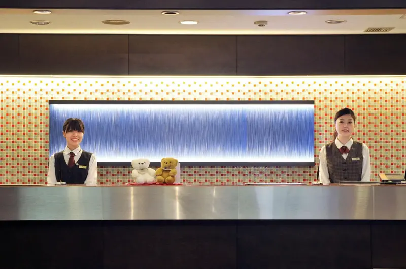 Deux employées souriantes se tiennent derrière un comptoir d'accueil décoré.