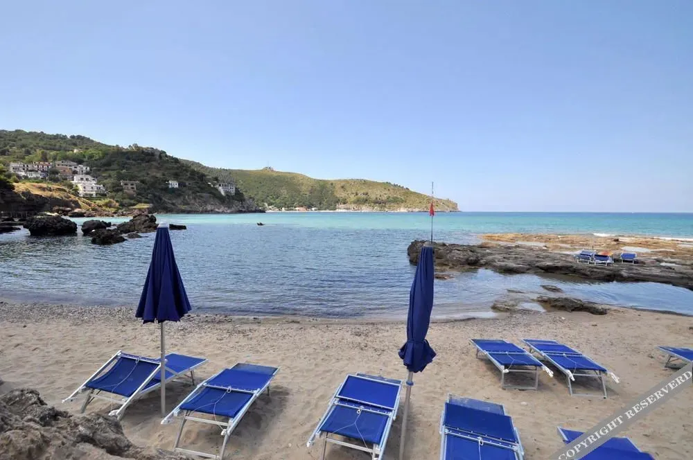 Plage de sable avec transats bleus et parasols face à une mer turquoise.