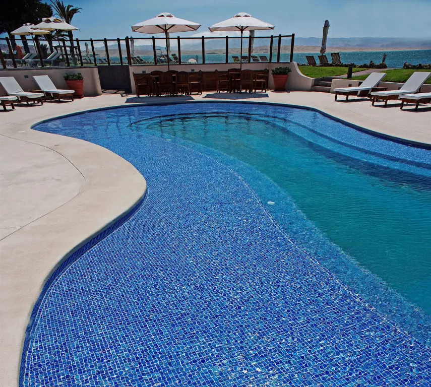 Une piscine bleue bordée d'une terrasse avec des transats et des parasols.