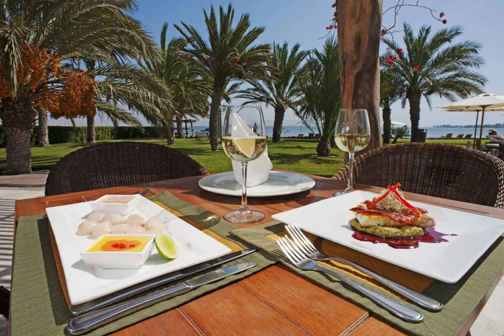 Une table est dressée avec des plats et des verres de vin sur une terrasse ensoleillée.