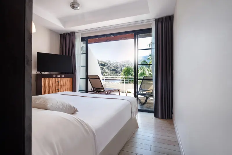 Une chambre lumineuse s'ouvre sur une terrasse avec vue sur la végétation.