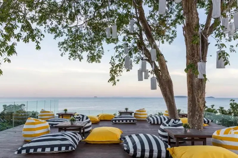 Espace de détente extérieur avec des coussins et des tables basses face à la mer.