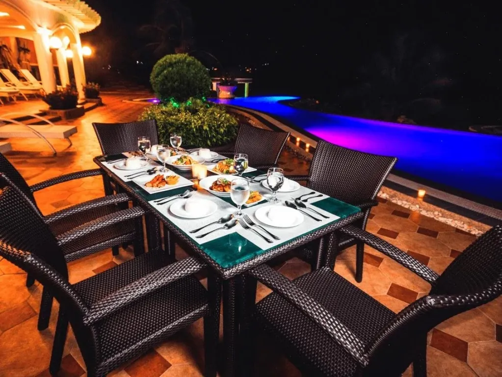 Une table de repas est dressée en extérieur, près d'une piscine illuminée.