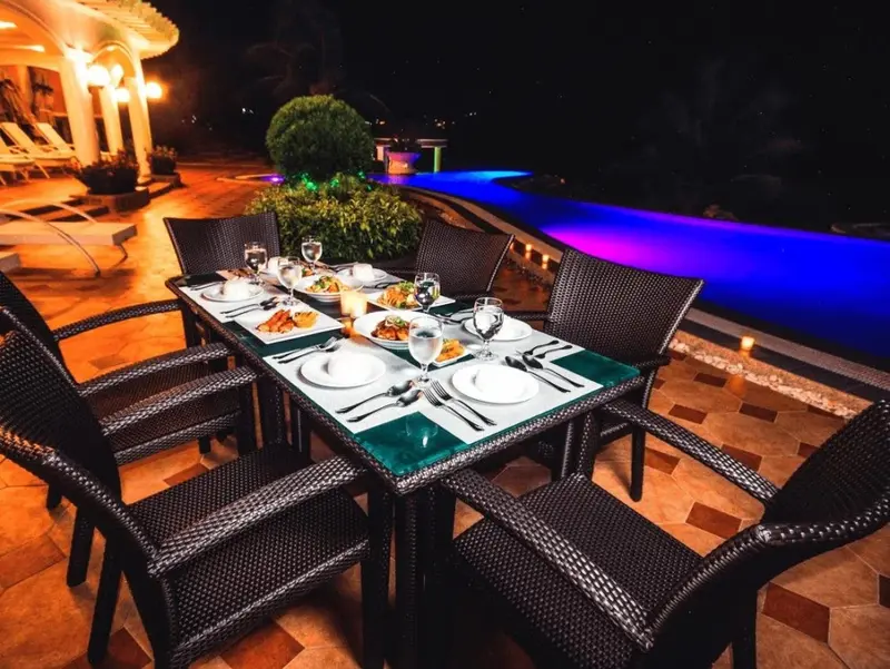 Une table de repas est dressée en extérieur, près d'une piscine illuminée.