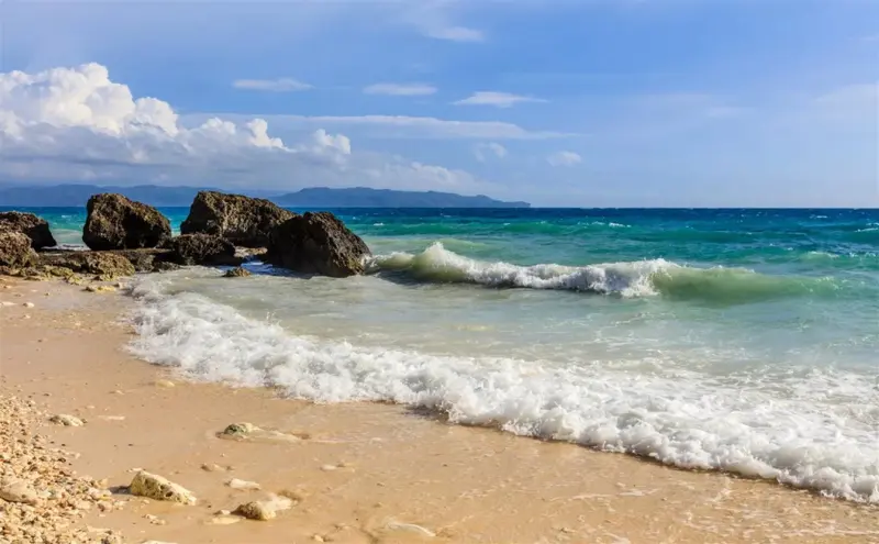 Une plage de sable fin bordée par une mer turquoise et des rochers.