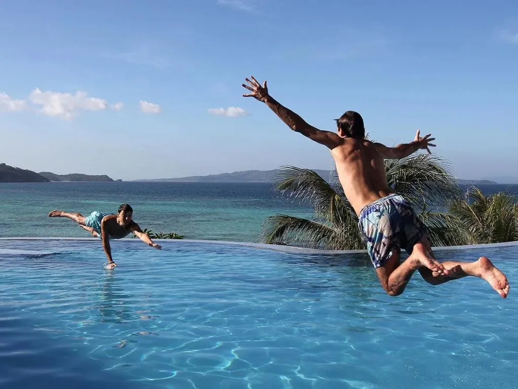 Deux personnes sautent dans une piscine à débordement avec vue sur la mer.