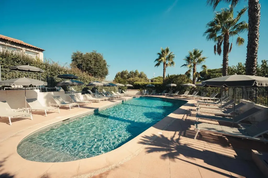 Une piscine rectangulaire bordée de transats sous des parasols, entourée de végétation luxuriante et de palmiers.