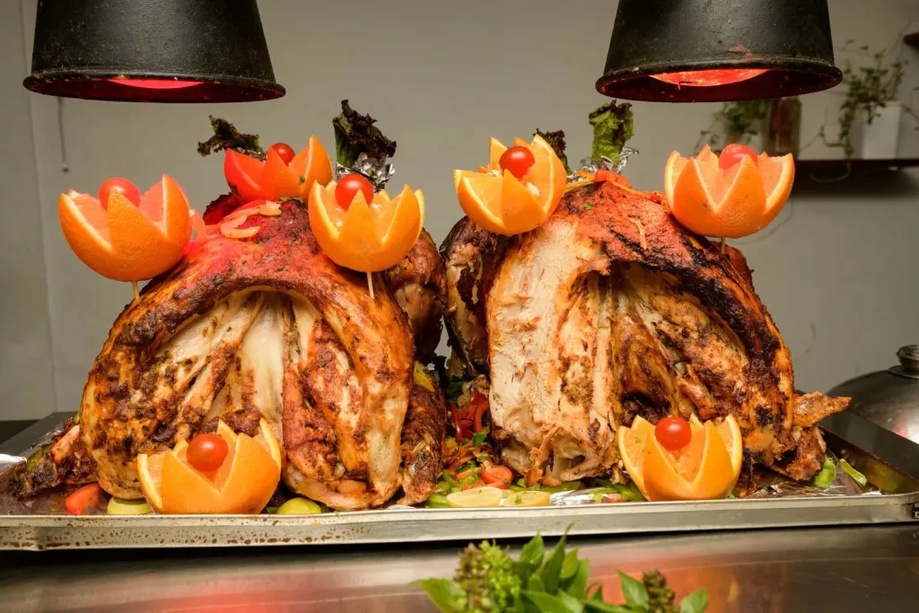 Deux pieces de viande rôtie, décorées d'oranges et de tomates, sont présentées sur un plateau.