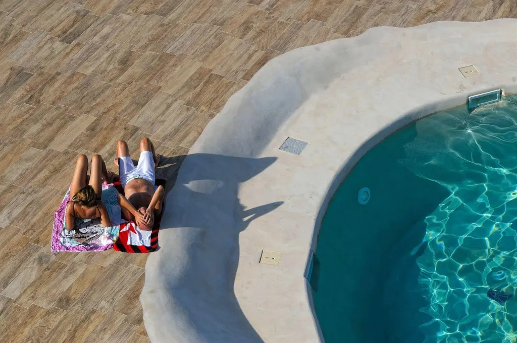 Deux personnes se relaxent au soleil près d'une piscine.