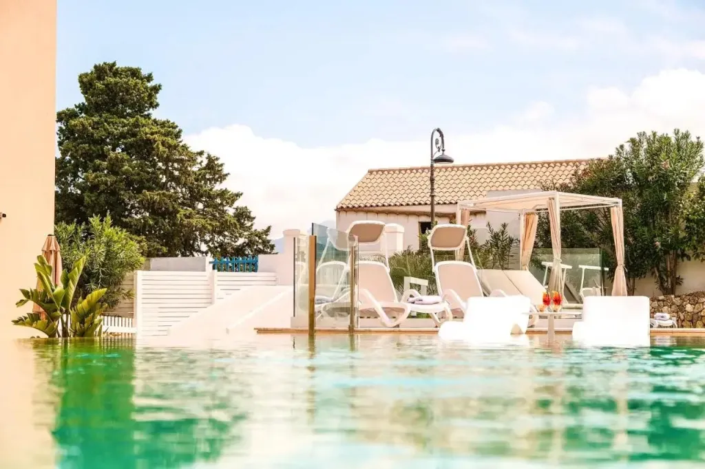 Transats blancs disposés autour d'une piscine turquoise et d'une pergola.