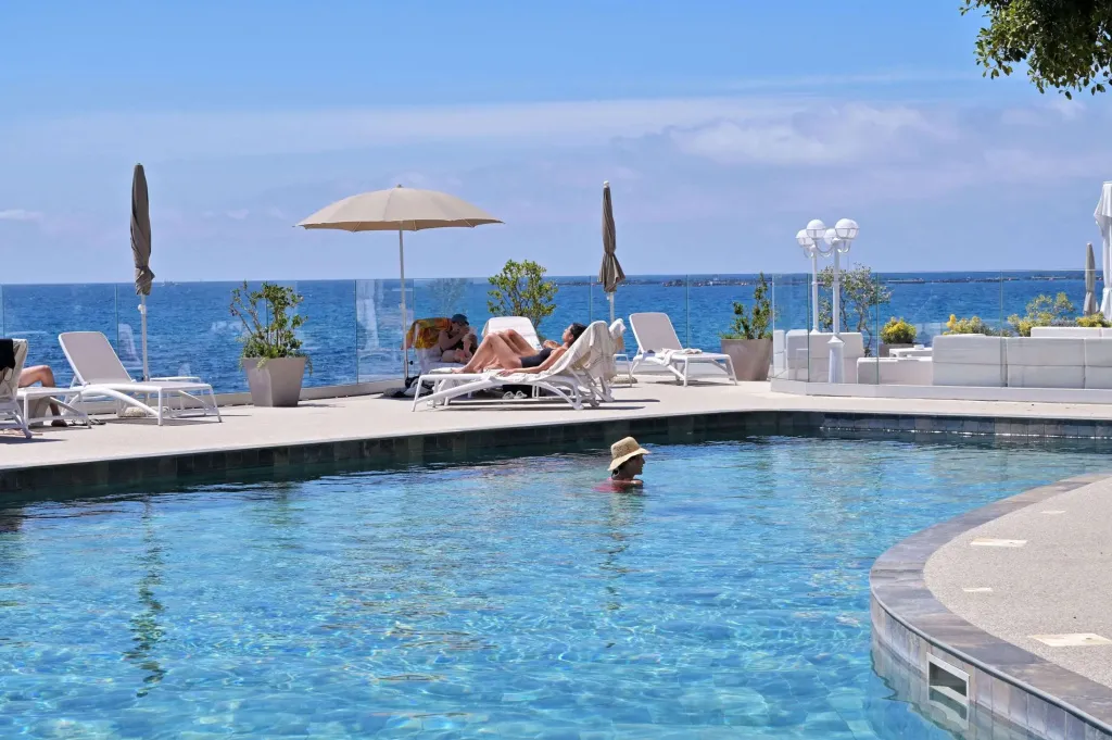 Une piscine bordée de transats sous des parasols, avec une vue sur la mer.